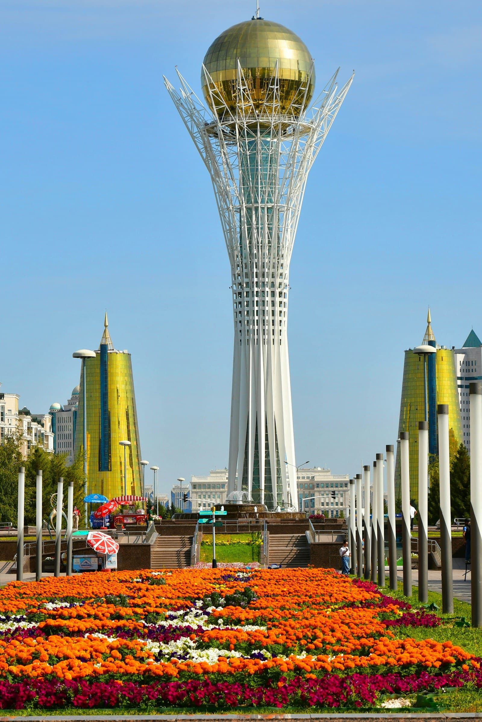 Kazakhstan: a very tall tower with a golden dome in the middle of a field of flowers