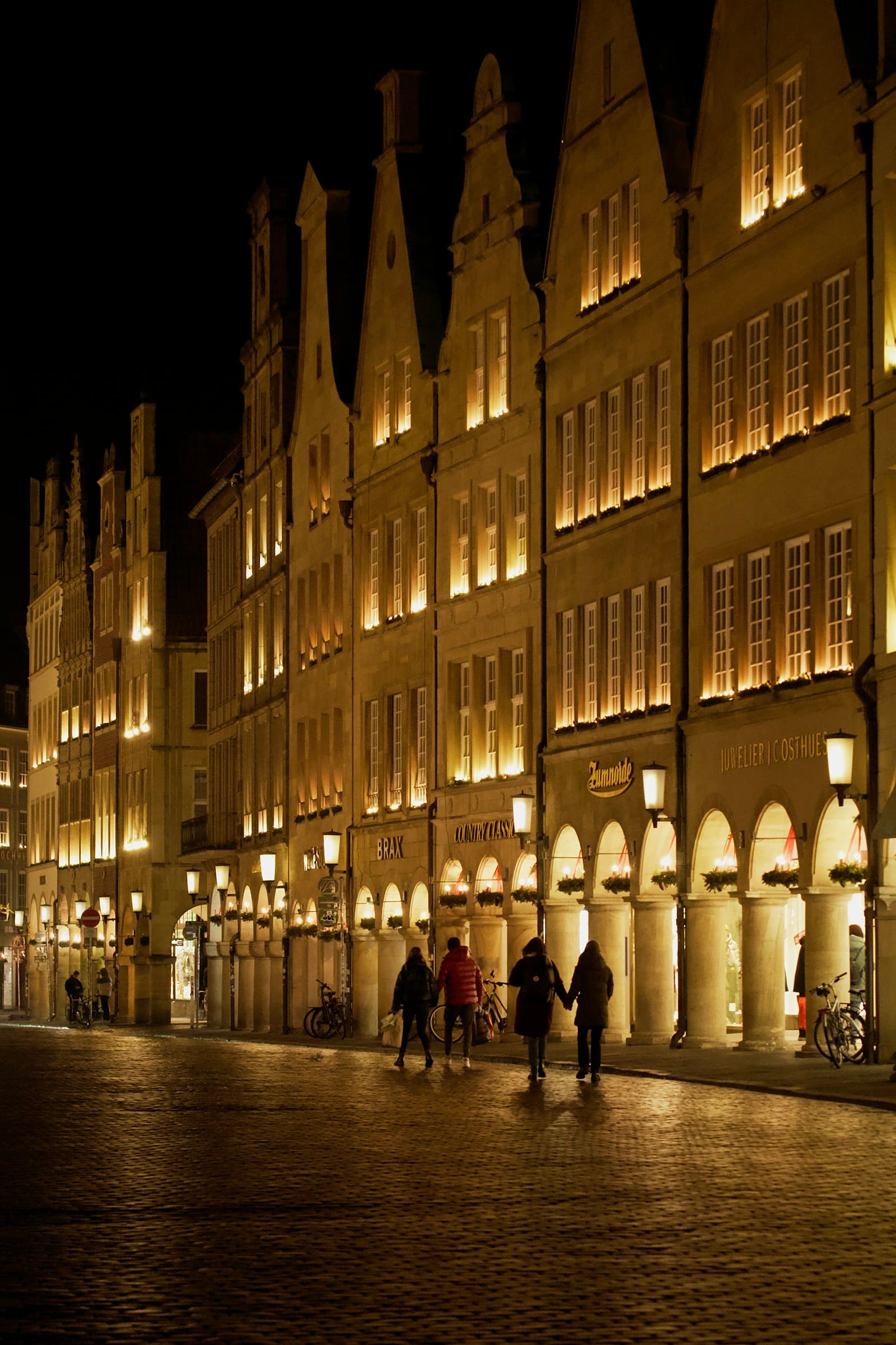 Munster: a group of people walking down a street next to tall buildings